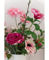 Eine Nahaufnahme der künstlichen Rose Real Touch 56 cm rosa, ein Strauß rosafarbener Kunstrosen mit grünen Blättern in einer weißen Vase, vor einem hellen Hintergrund.