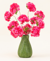 Eine grüne Vase mit Blattmotiv zeigt den künstlichen Seidenblumenstrauß Cherry Blossom Pink – leuchtend rosa, flauschige Seidenkirschblüten mit grünen Blättern – vor einem schlichten hellen Hintergrund.