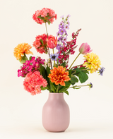 Het Zijden kunstbloemen boeket Colourburst Blossom heeft een pastelroze vaas gevuld met oranje dahlia's, roze anjers, gele dahlia's, paarse riddersporen en rode tulpen-ideale kunstboeket decoratie voor elke kamer.