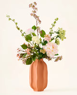 In einer pfirsichfarbenen Keramikvase befindet sich ein Strauß rosa-weißer Kunstblumen aus Seide, der „Dreamy Meadow“-Strauß, mit grünen Blättern und Stielen vor einem schlichten, hellen Hintergrund.