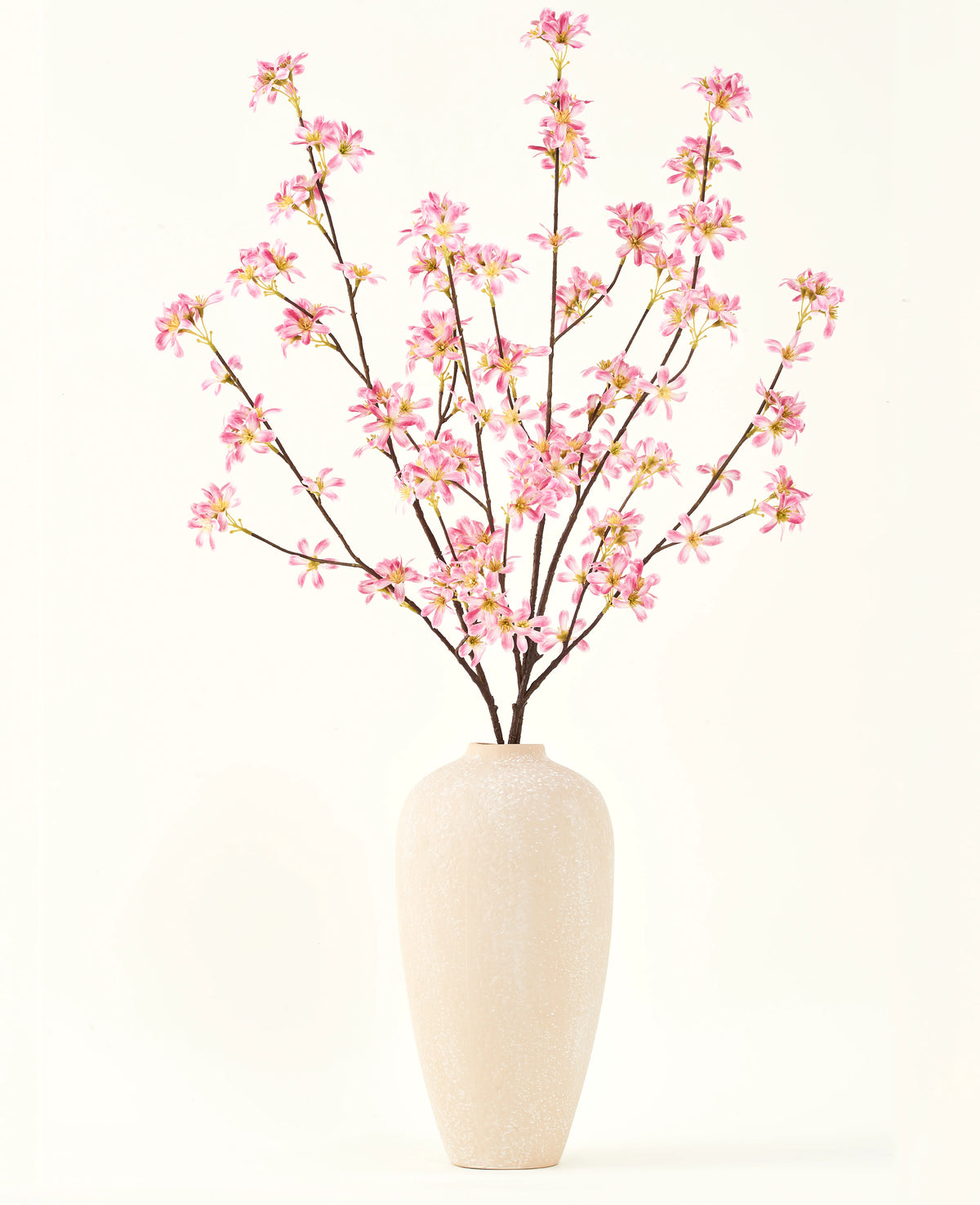 Eine hohe beige Keramikvase enthält mehrere Zweige des künstlichen Blumenstraußes aus Seide. Rosa Blumen mit zartrosa Blüten und grünen Blättern vor einem schlichten weißen Hintergrund.