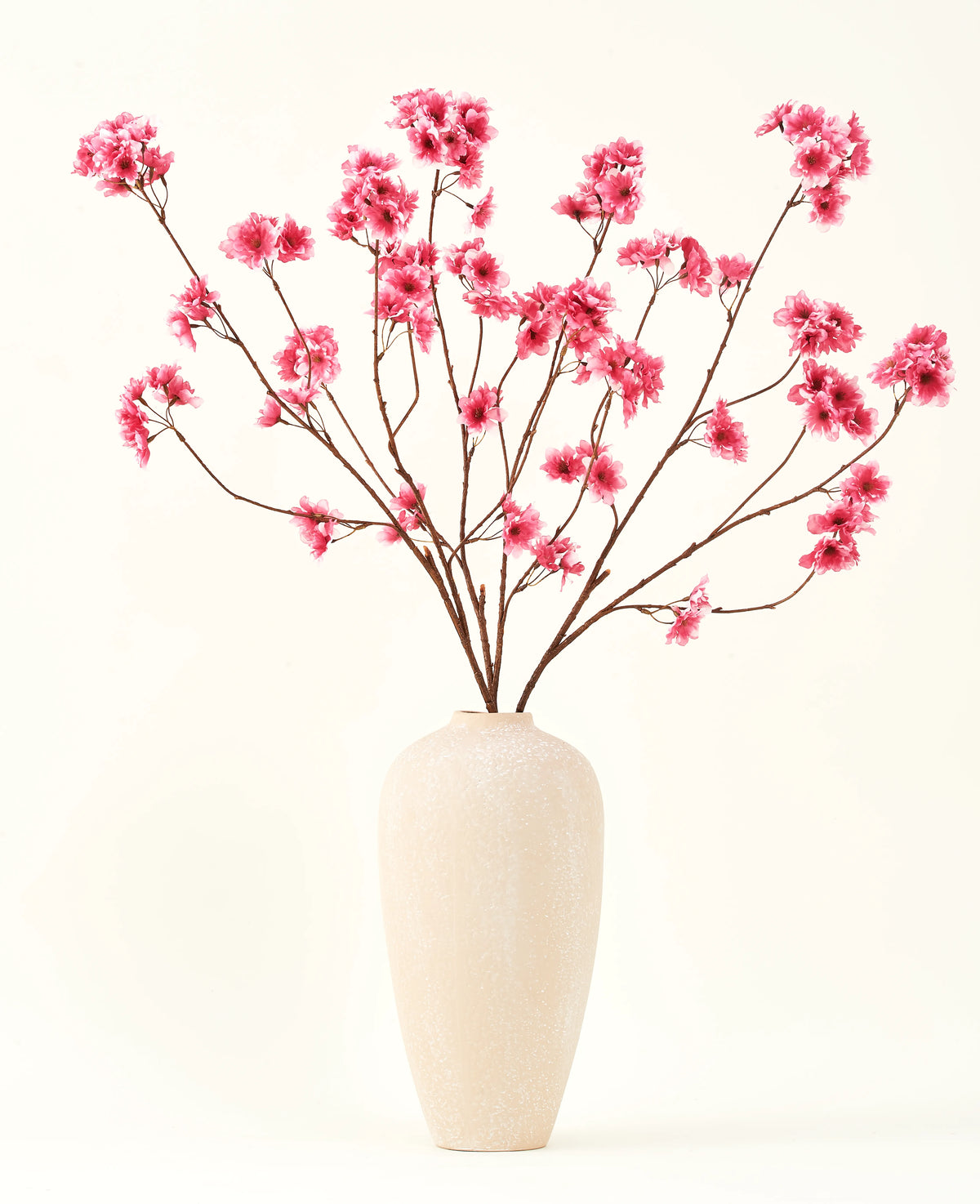 Der künstliche Blumenstrauß aus Seide, Kirschblüten-Fuchsia, 114 cm, verleiht Ihrem Interieur mit seinen markanten Zweigen und fuchsiafarbenen Blüten, die wunderschön in einer beigen Keramikvase vor einem schlichten, cremefarbenen Hintergrund zur Geltung kommen, einen lebendigen Farbtupfer.