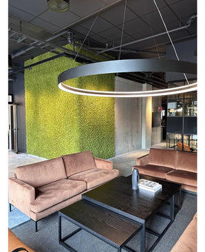 Eine moderne Sitzecke mit beigen Sofas, schwarzen Couchtischen, einer großen runden Deckenlampe und einer grünen Wand im Hintergrund, gestaltet mit Kunsthaag Nordic Moss 50x50 cm UV, die ein luxuriöses Interieur und ein zeitgenössisches Industriedesign ausstrahlt.