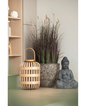 Auf einer hellen Fläche, in der Nähe eines Holzregals und einer hellen Wand, sind eine Holzlaterne, ein hoher Steintopf mit 100 cm künstlichem Zwiebelgras-Bonsai (feuerhemmend) und eine graue Buddha-Statue angeordnet.
